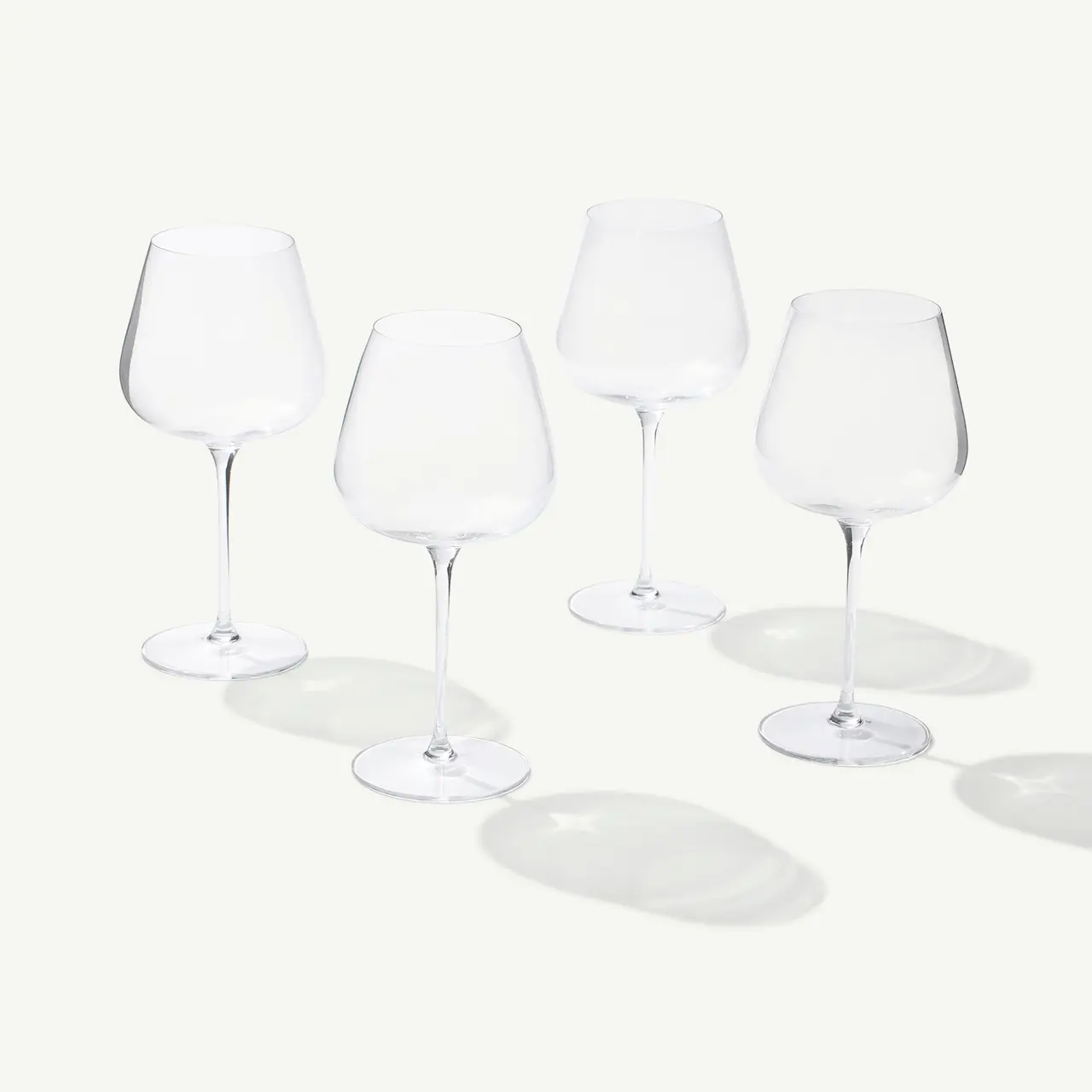 Four empty wine glasses casting soft shadows on a light surface.