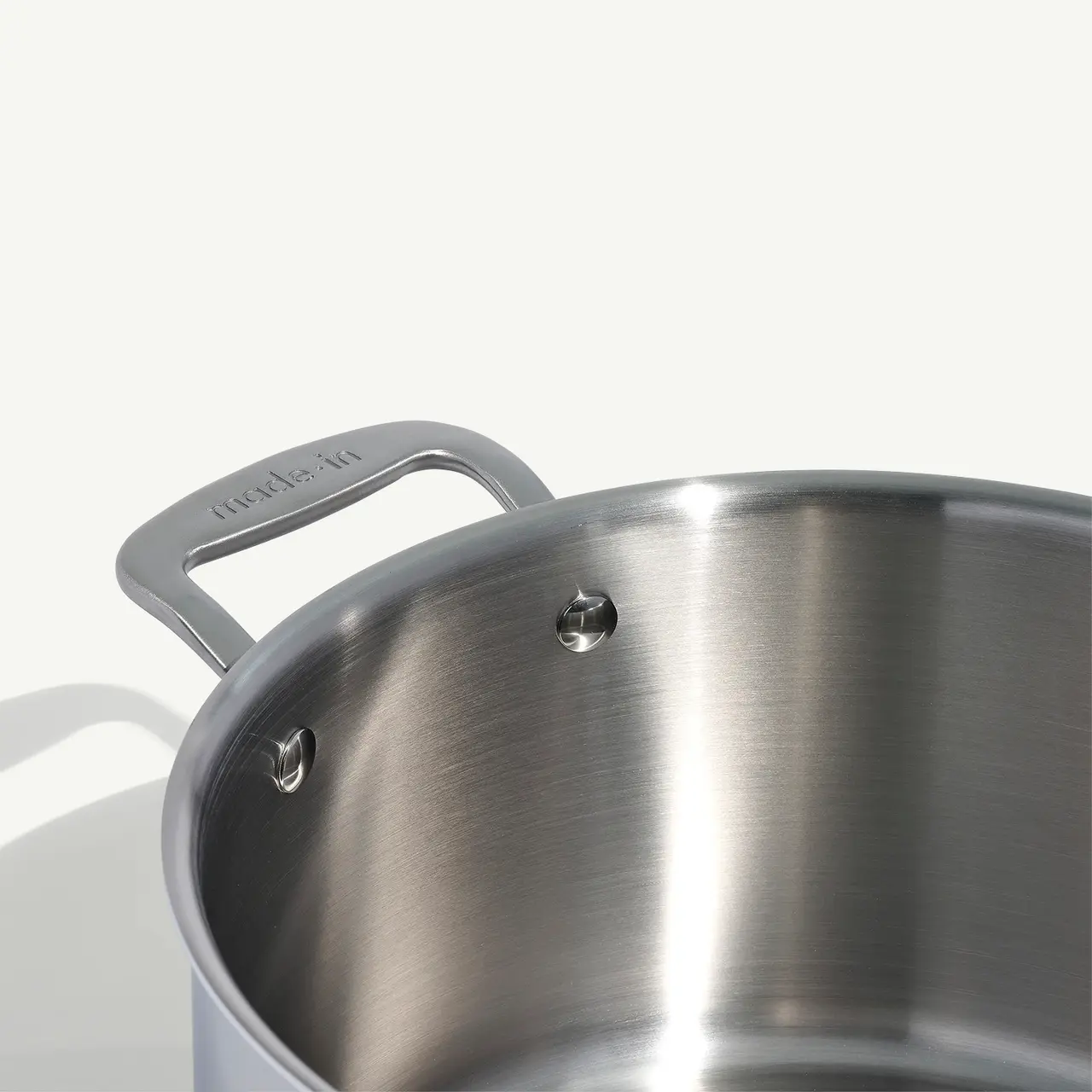 A close-up of a stainless steel pot showing a riveted handle with the brand name.