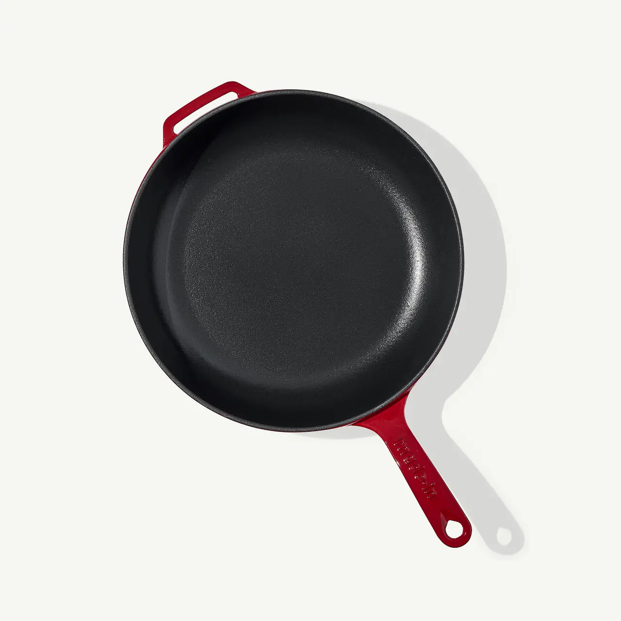 A black cast iron skillet with a red handle is positioned on a light gray background.