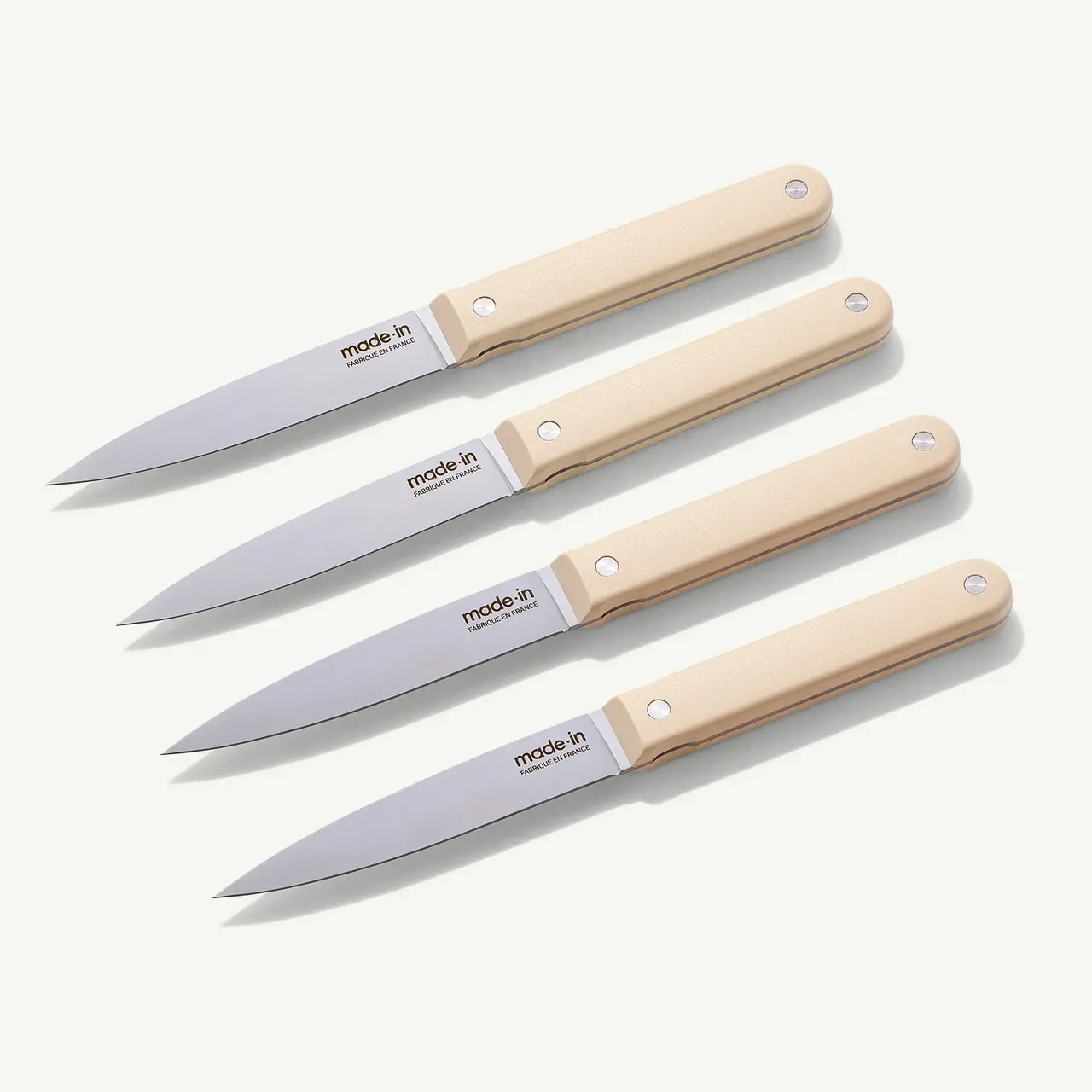 Four identical kitchen knives with beige handles are neatly aligned on a light background.