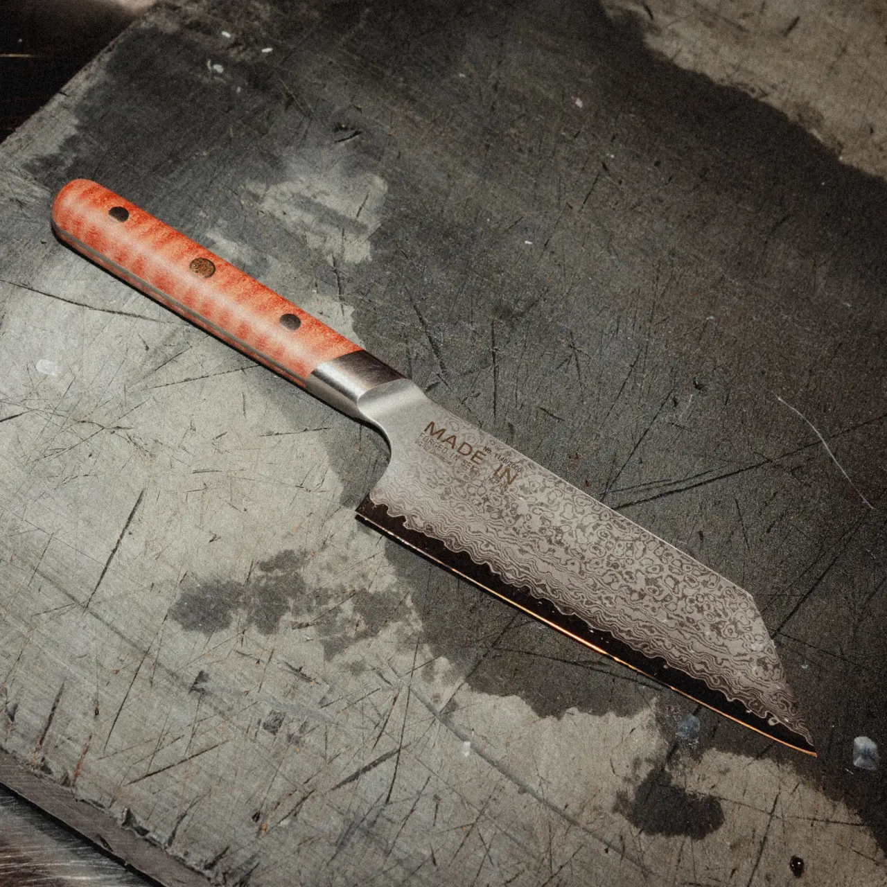 A sharp, serrated knife with a wooden handle rests on a textured wooden cutting board.
