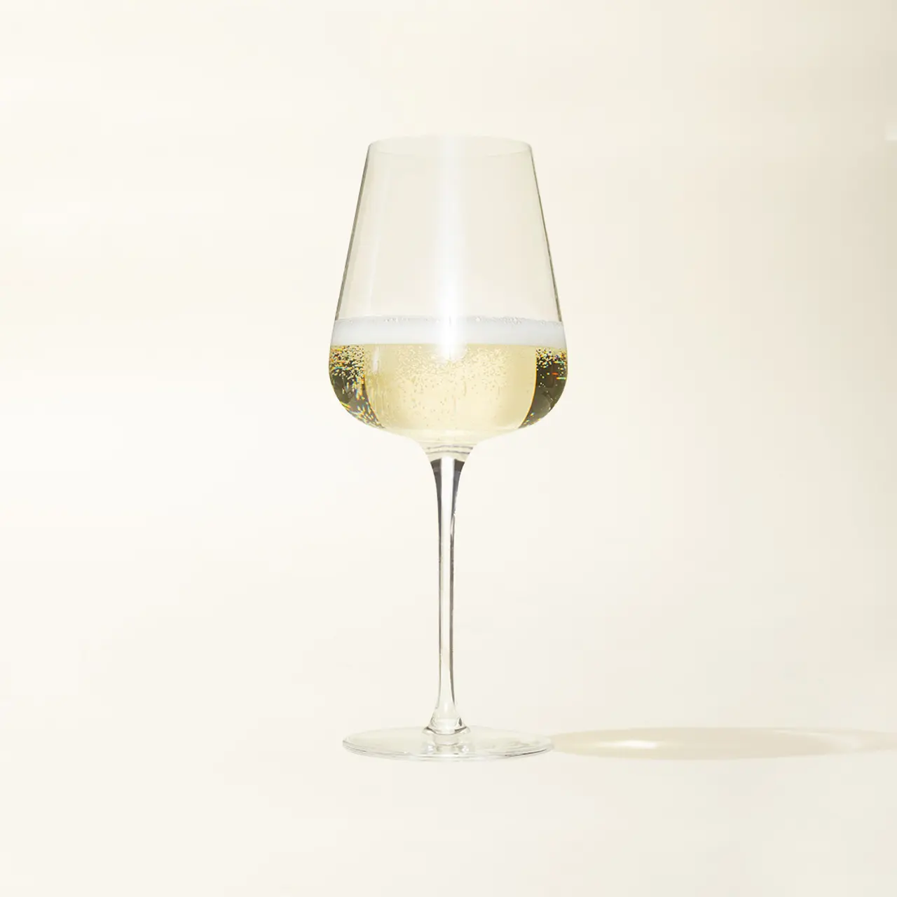 A glass of sparkling wine is set against a plain background, capturing the effervescence and clarity of the beverage.