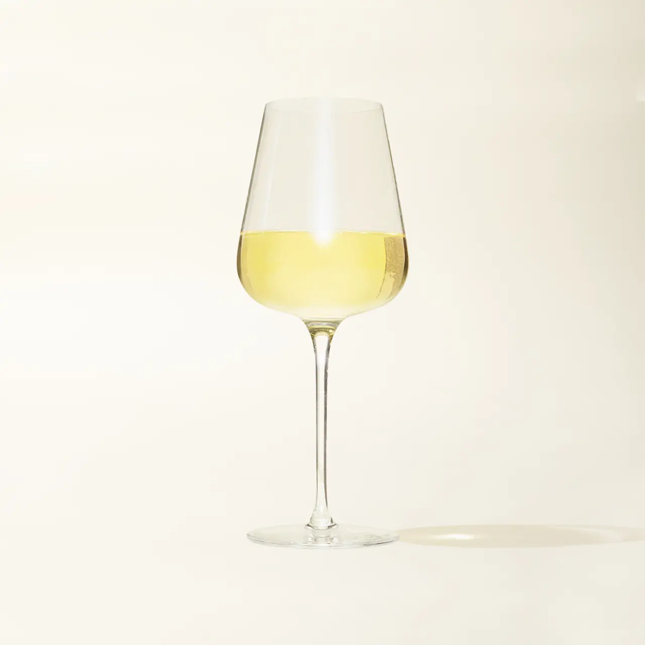 A wine glass half-filled with white wine stands against a neutral background.