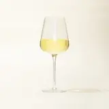 A wine glass half-filled with white wine stands against a neutral background.