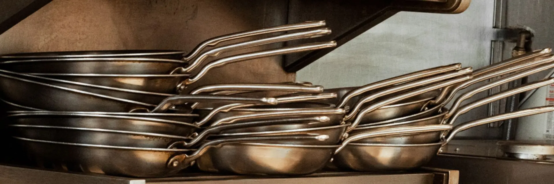 A stack of stainless steel frying pans with metal handles.