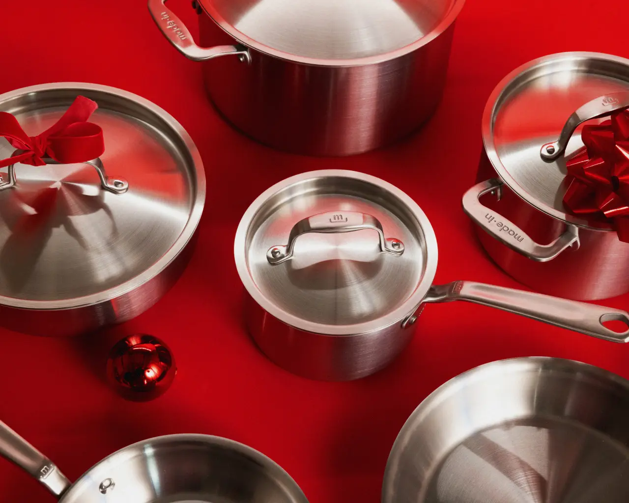 Stainless steel cookware pieces are arranged on a red background, adorned with festive red bows and a shiny red ornament.