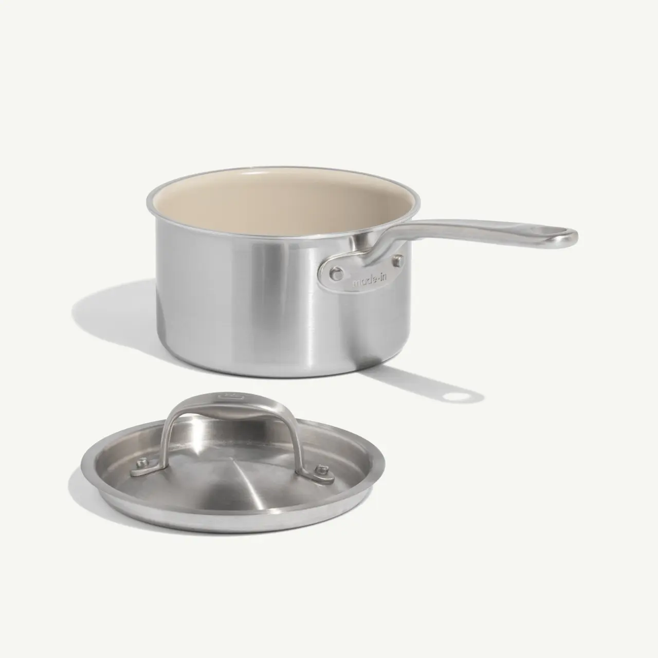 A stainless steel saucepan with an attached handle sits beside its matching lid.