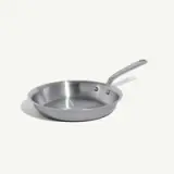 A stainless steel frying pan is isolated on a light background.