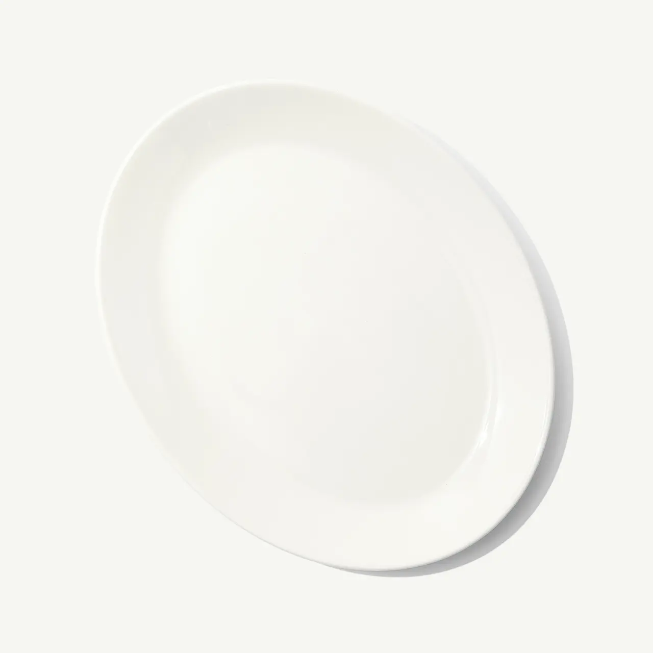 An empty white oval plate is centered on a plain background.