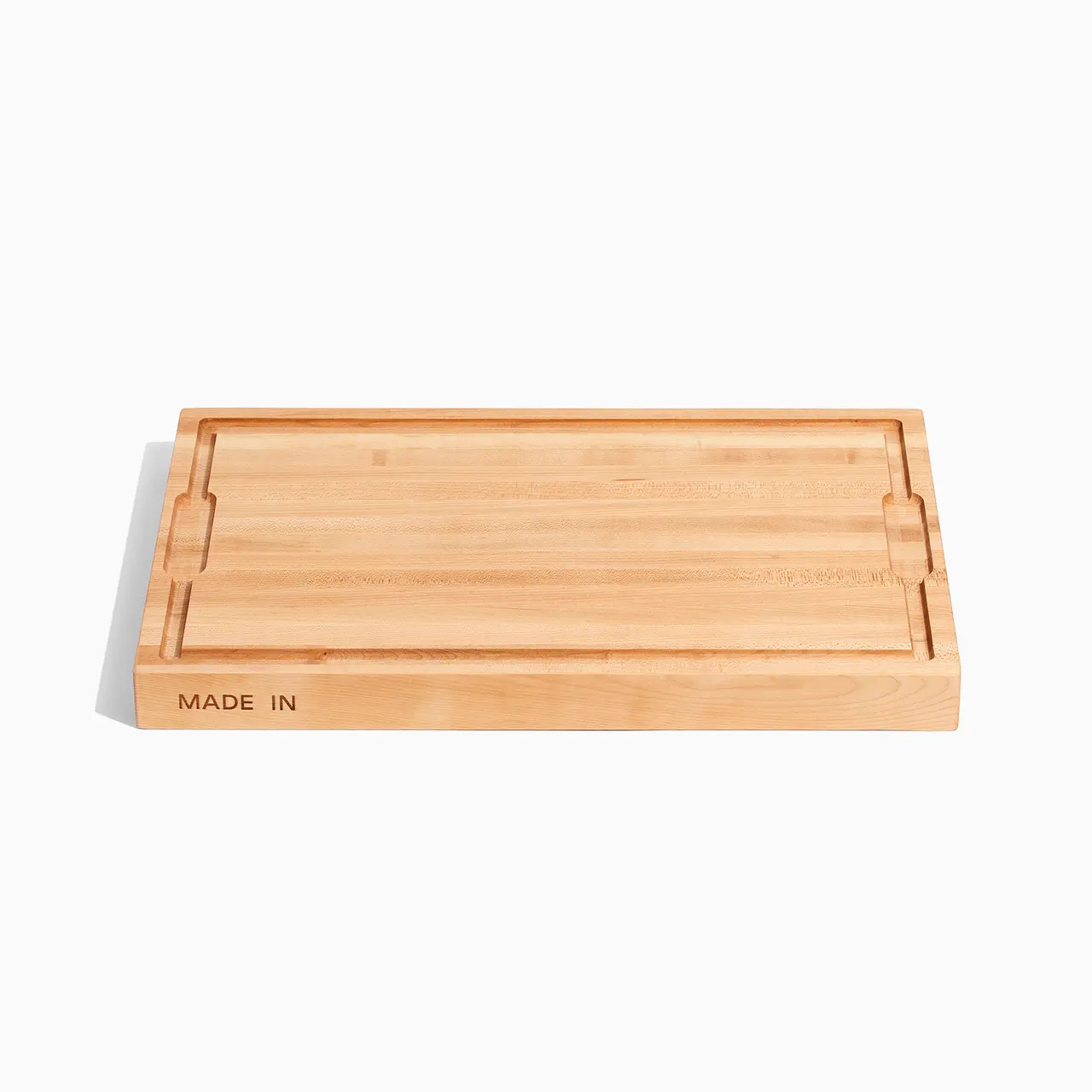 A rectangular bamboo cutting board with a juice groove on the perimeter and the words "MADE IN" inscribed on one side.
