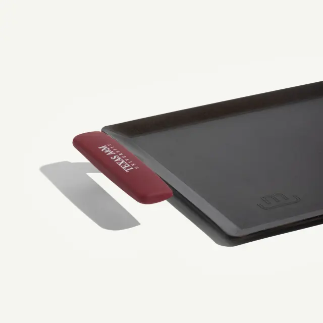 A rectangular cooking pan with a red handle, designed for grilling or baking.