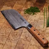 A stainless steel kitchen knife with a wooden handle and a serrated edge is placed on a wooden cutting board, surrounded by chopped herbs.