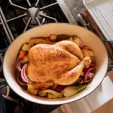 A seasoned whole chicken sits atop a bed of mixed vegetables in a large cooking pot.