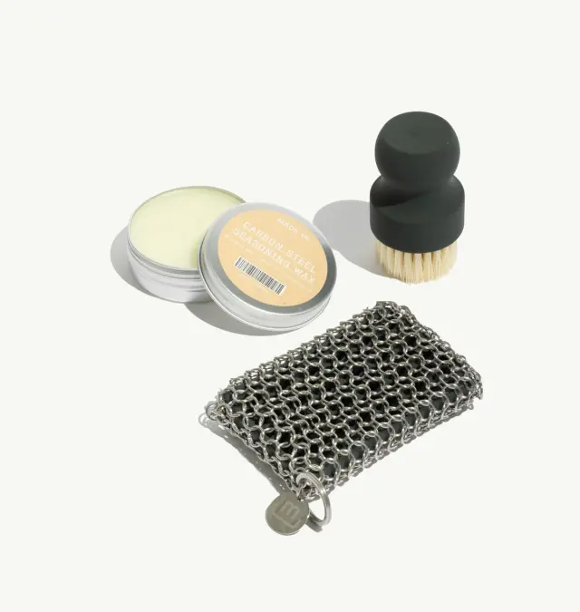 A small collection of personal care items, including a tin of balm, a scrub brush with a round handle, and a metal chain mesh cleaning cloth.