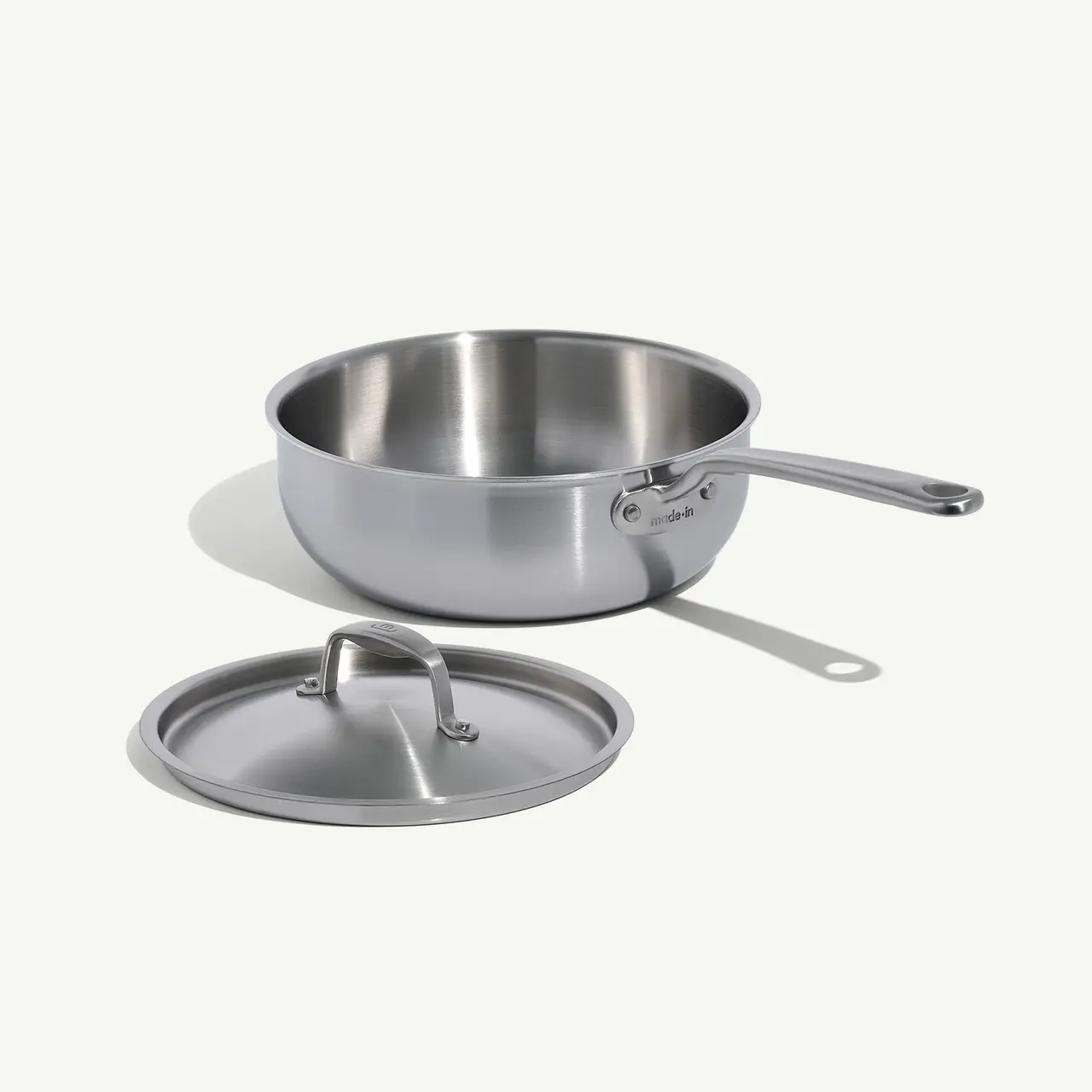 A stainless steel saucepan with a long handle is shown next to its matching lid on a light background.