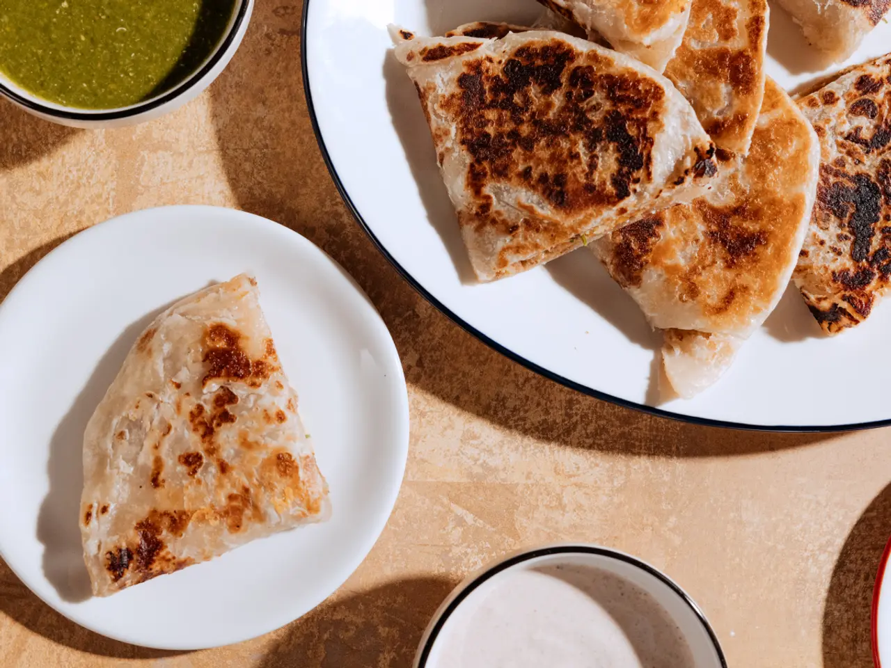 Several pieces of golden-brown flatbread are served on plates with a side of green sauce.