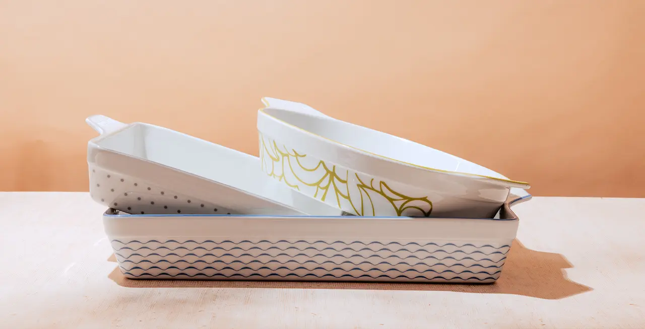 Stacked ceramic baking dishes on a table against a peach-colored backdrop.