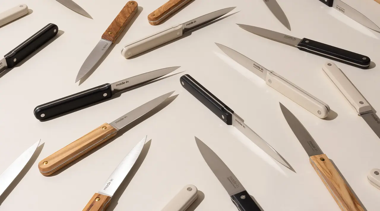 A collection of various kitchen knives with different handles and blade shapes arranged haphazardly on a light surface.