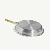 A stainless steel frying pan is displayed upside down showcasing its bottom surface and a gold-colored handle against a light background.
