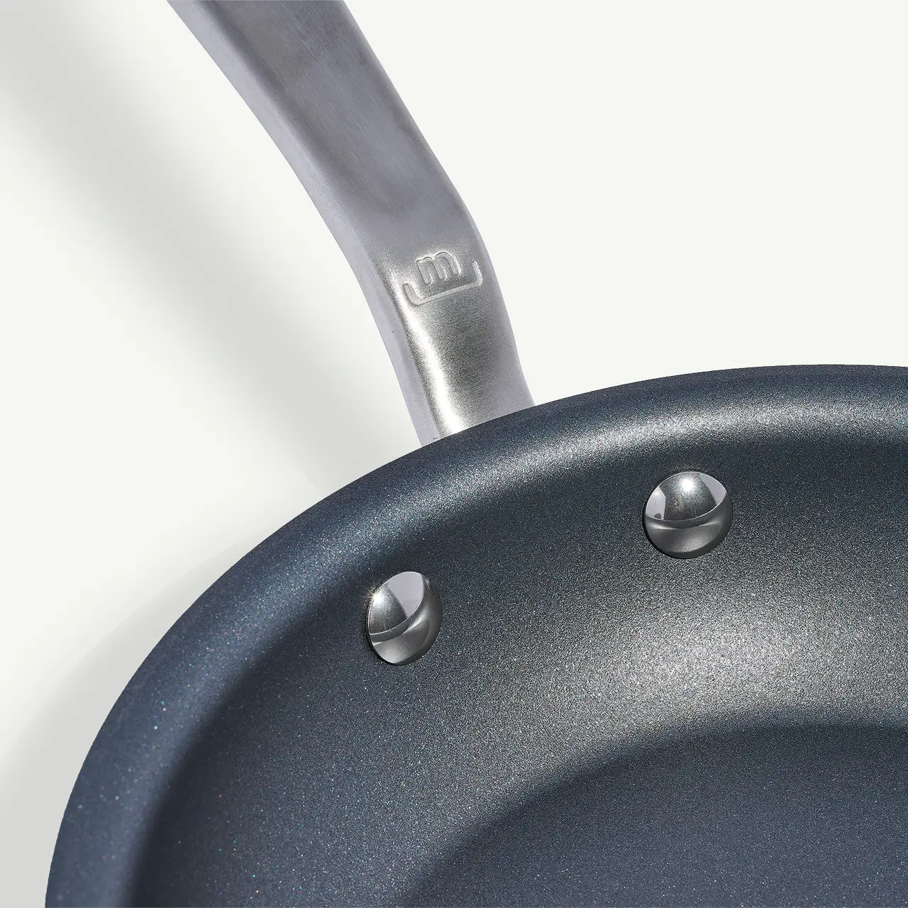 A close-up of a non-stick frying pan with a metal handle, focusing on the interior surface and rivets attaching the handle.