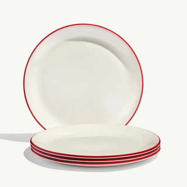 A stack of white plates with red trim is shown against a light background, one plate standing upright behind the stack.