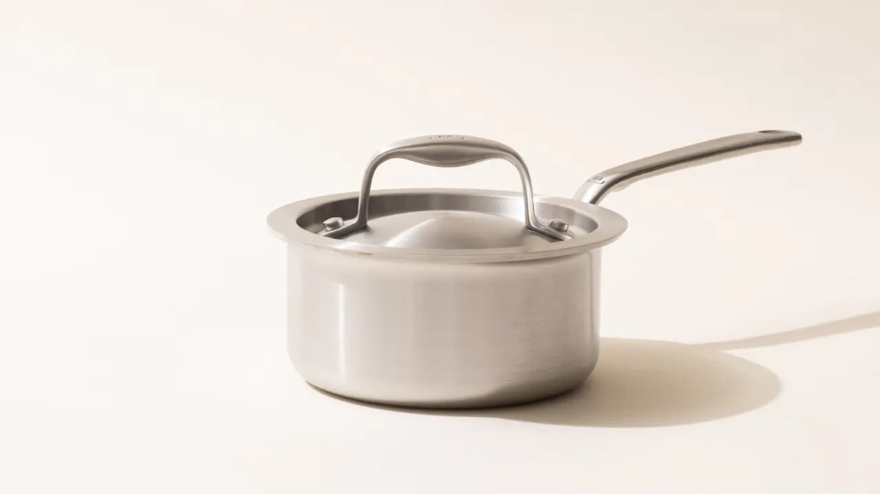 A stainless steel saucepan with a long handle on a light background, casting a soft shadow to the right.