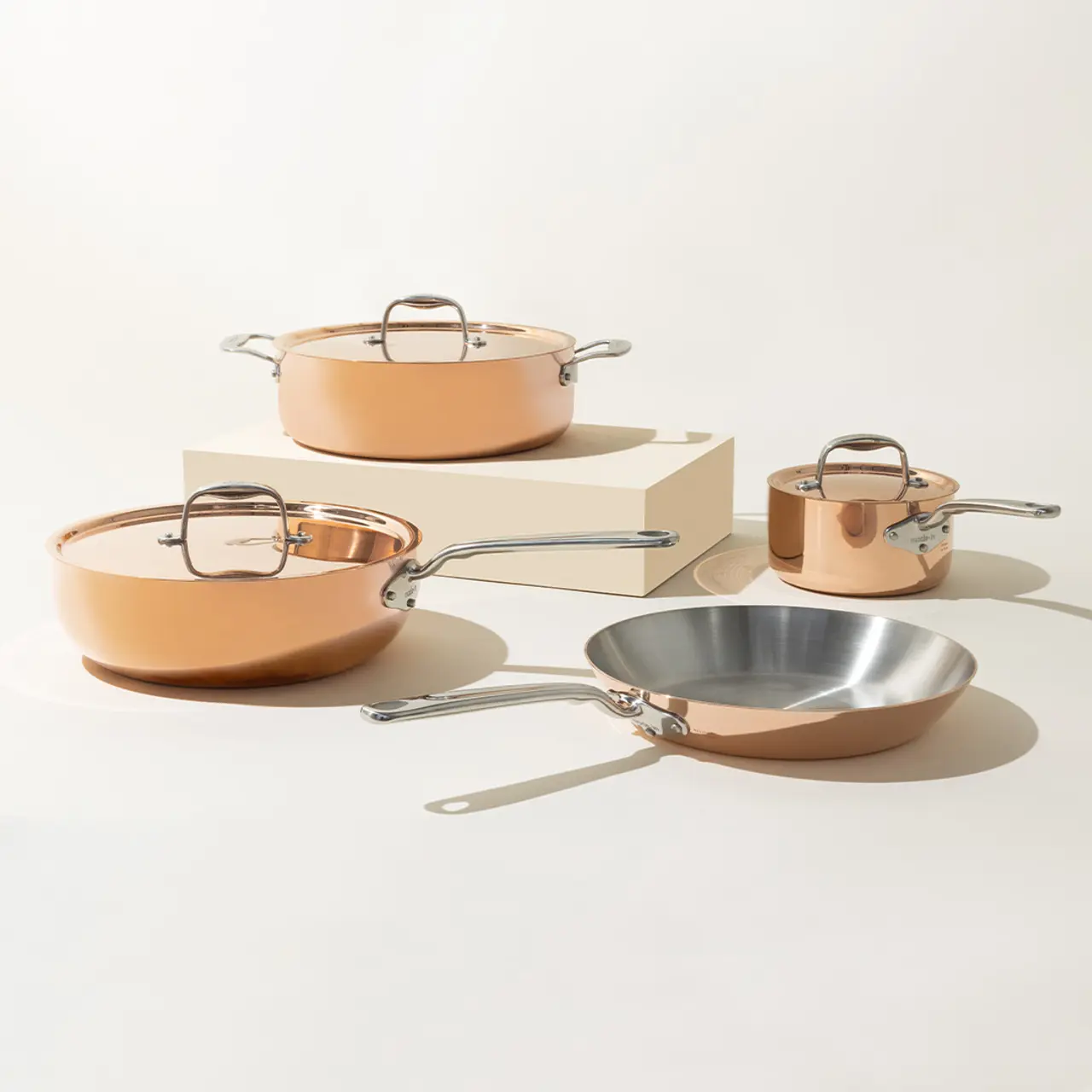 A set of elegant copper-colored cookware, including two pots with lids, a saucepan, and a skillet, artistically arranged on a neutral background.