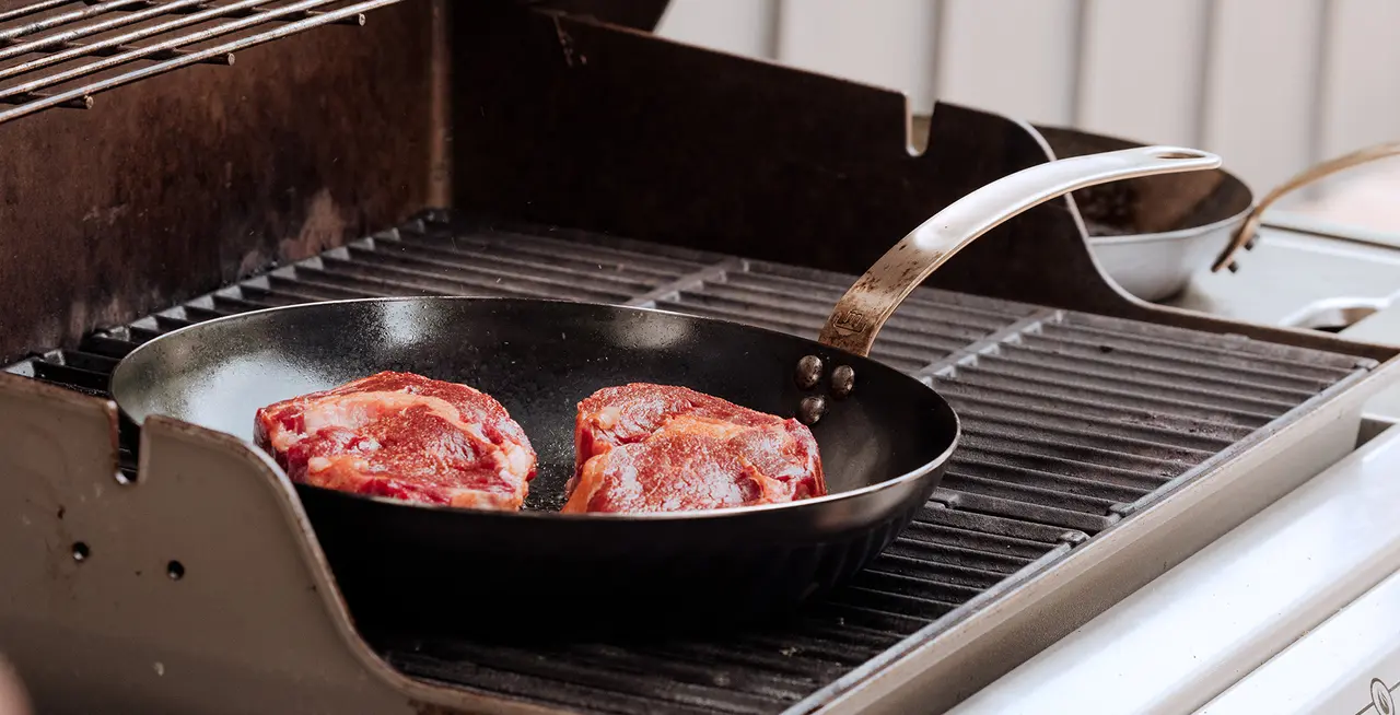 steak in carbon steel pan on grill