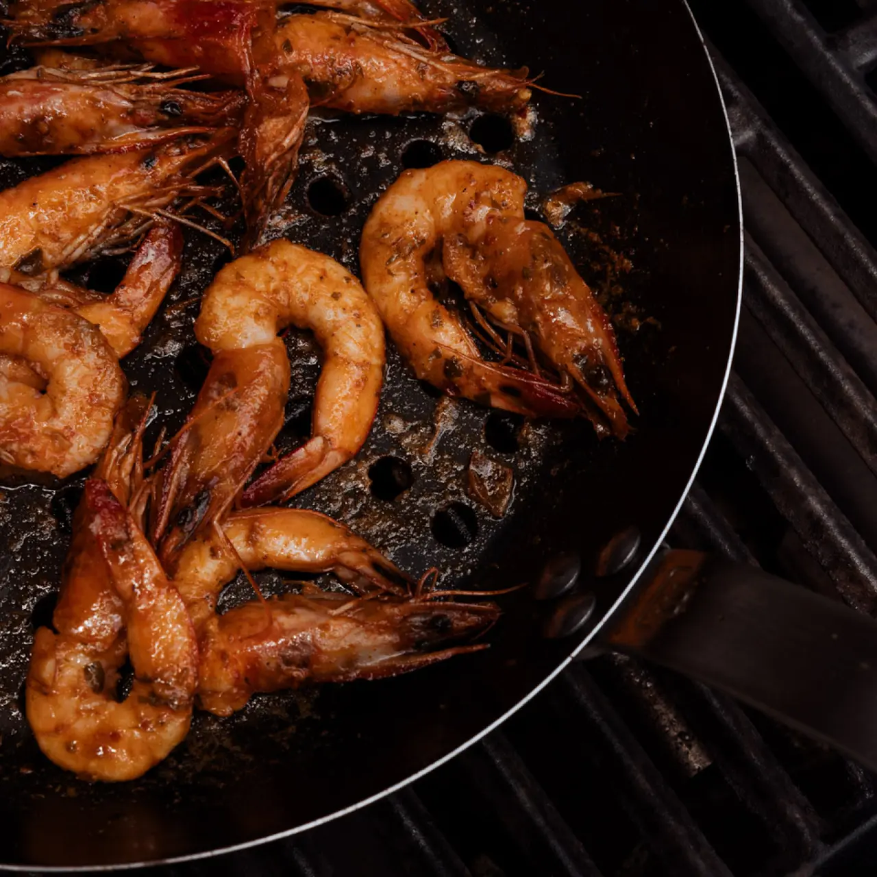 Shrimp are being sautéed in a black pan over a stovetop.