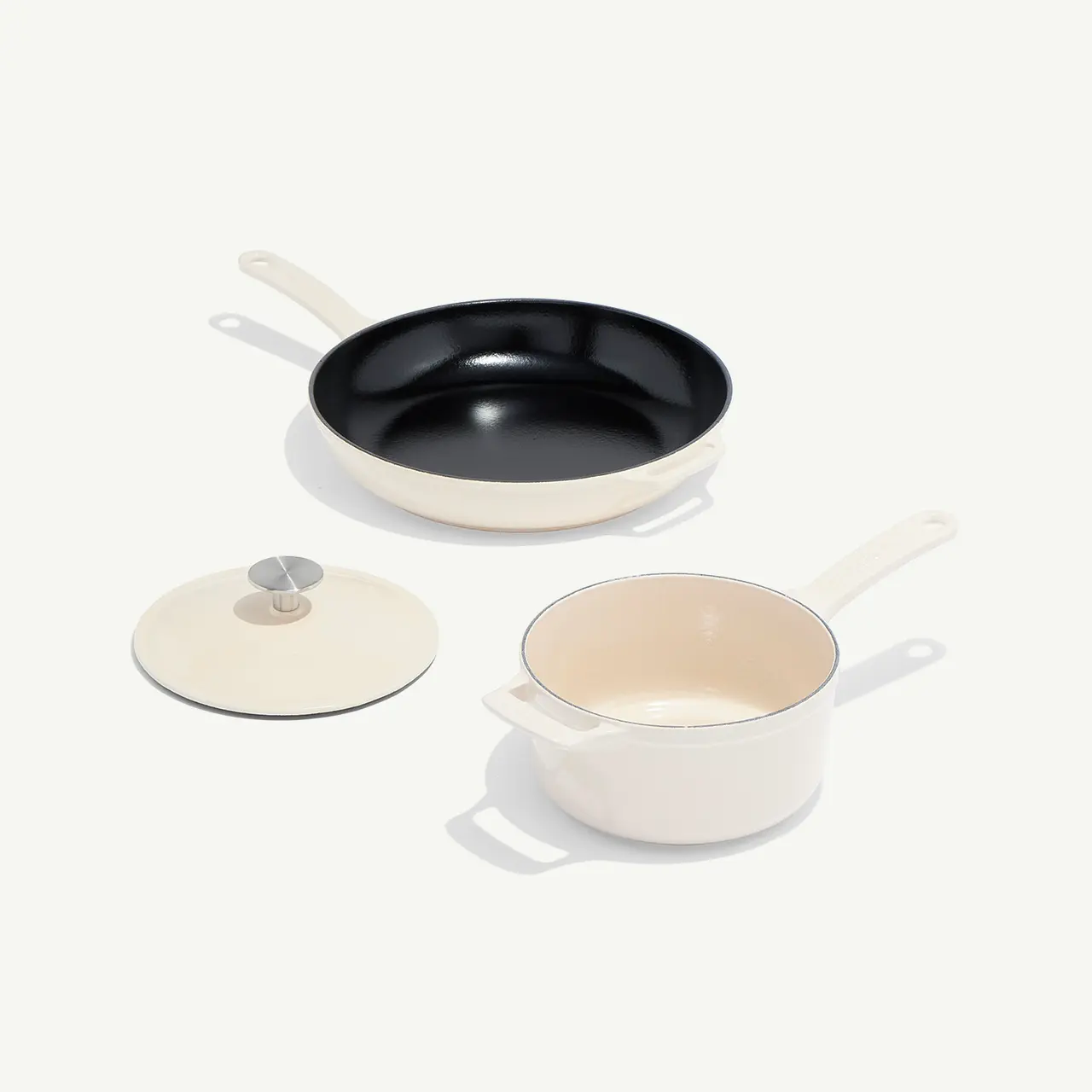 A black frying pan and a white saucepan with a matching lid are arranged neatly on a white background.