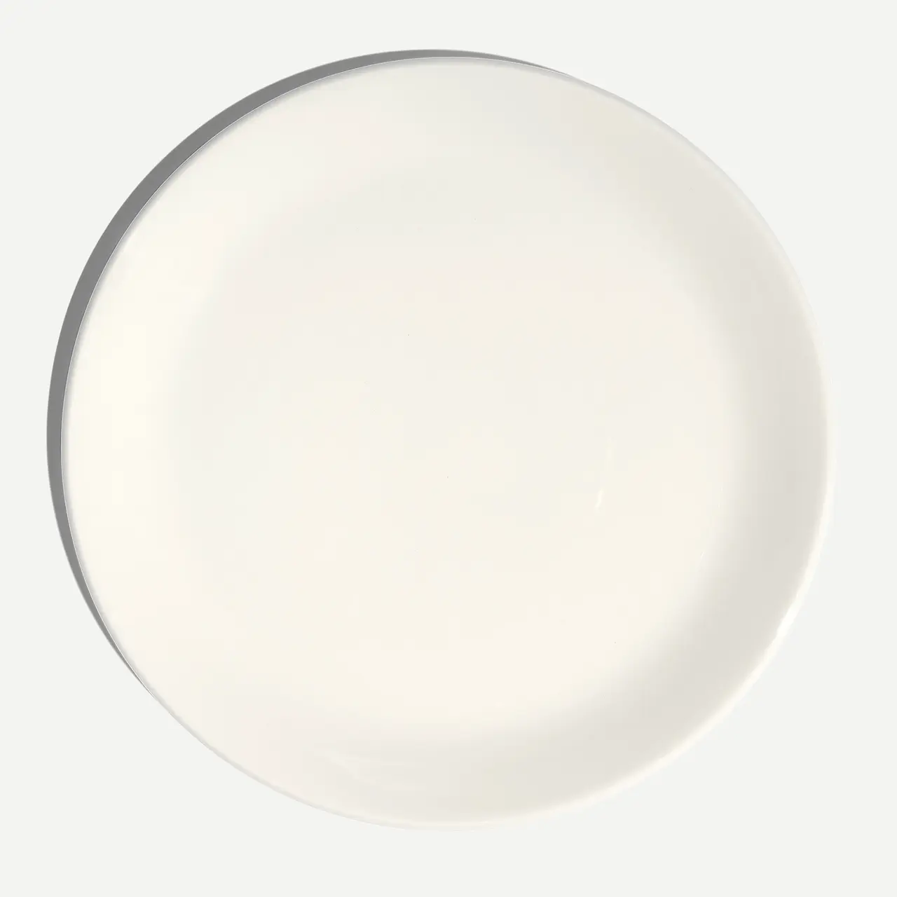 An empty white round plate is presented against a light background.