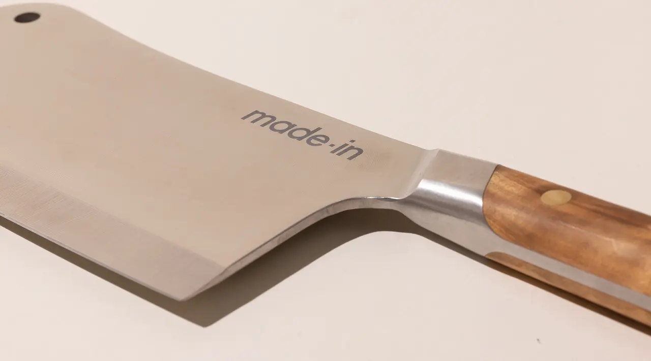 A close-up of a chef's knife with a stainless steel blade and wooden handle, with the text "made.in" engraved on the blade.