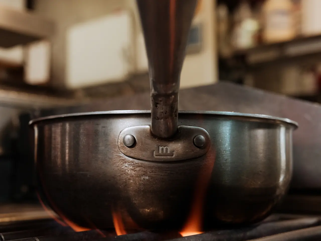 A saucepan heats up on a gas stove with flames licking the bottom.