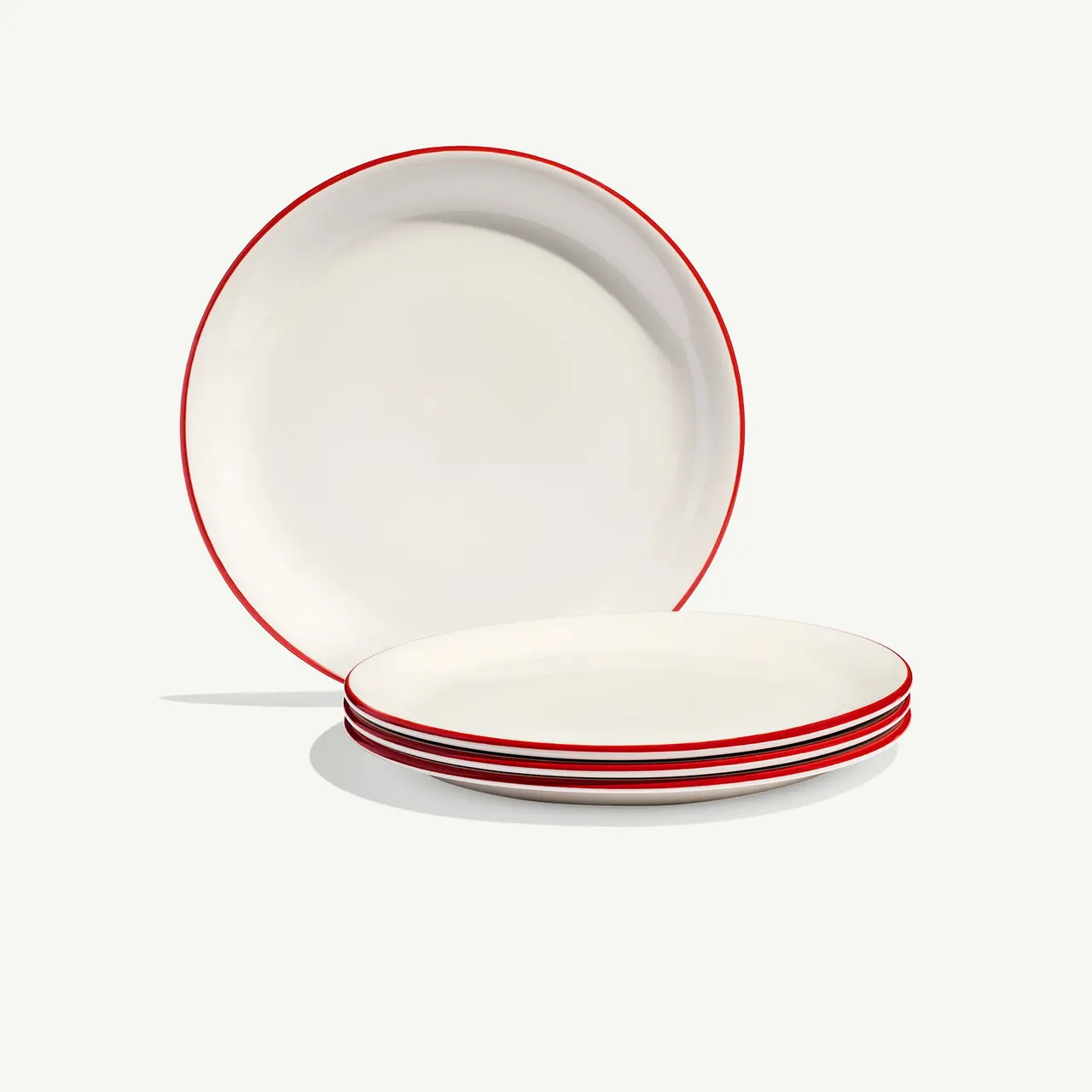A stack of white plates with red trim sits beside a single plate propped up on its edge against a light background.
