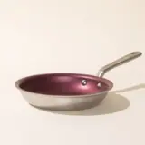 A single metal frying pan with a red interior and a silver handle, casting a shadow on a light background.