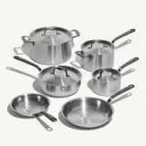 A set of stainless steel cookware, including pots with lids and two frying pans, arranged on a light background.