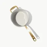 A silver pot with a gold handle sits against a light background, casting a shadow.