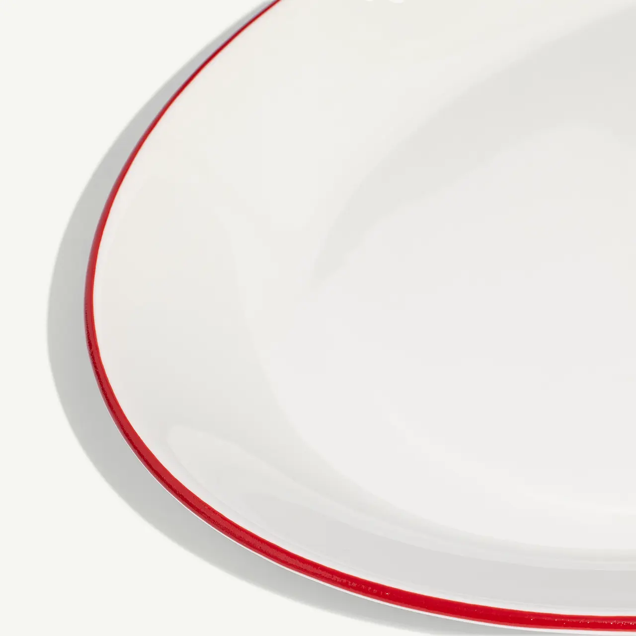 A close-up of a white plate with a red rim on a white background.