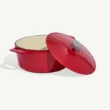 A red enameled cast iron Dutch oven with its lid slightly askew, against a white background.