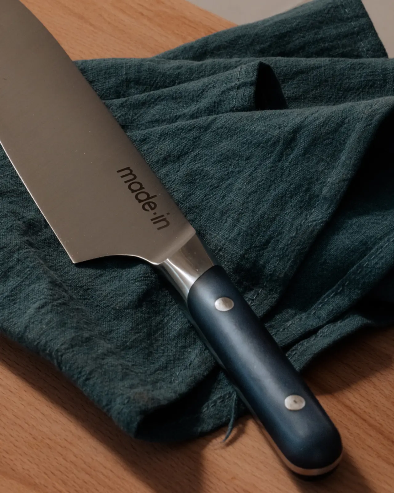 A close-up view of a chef's knife with a black handle laying on a crumpled dark green cloth.