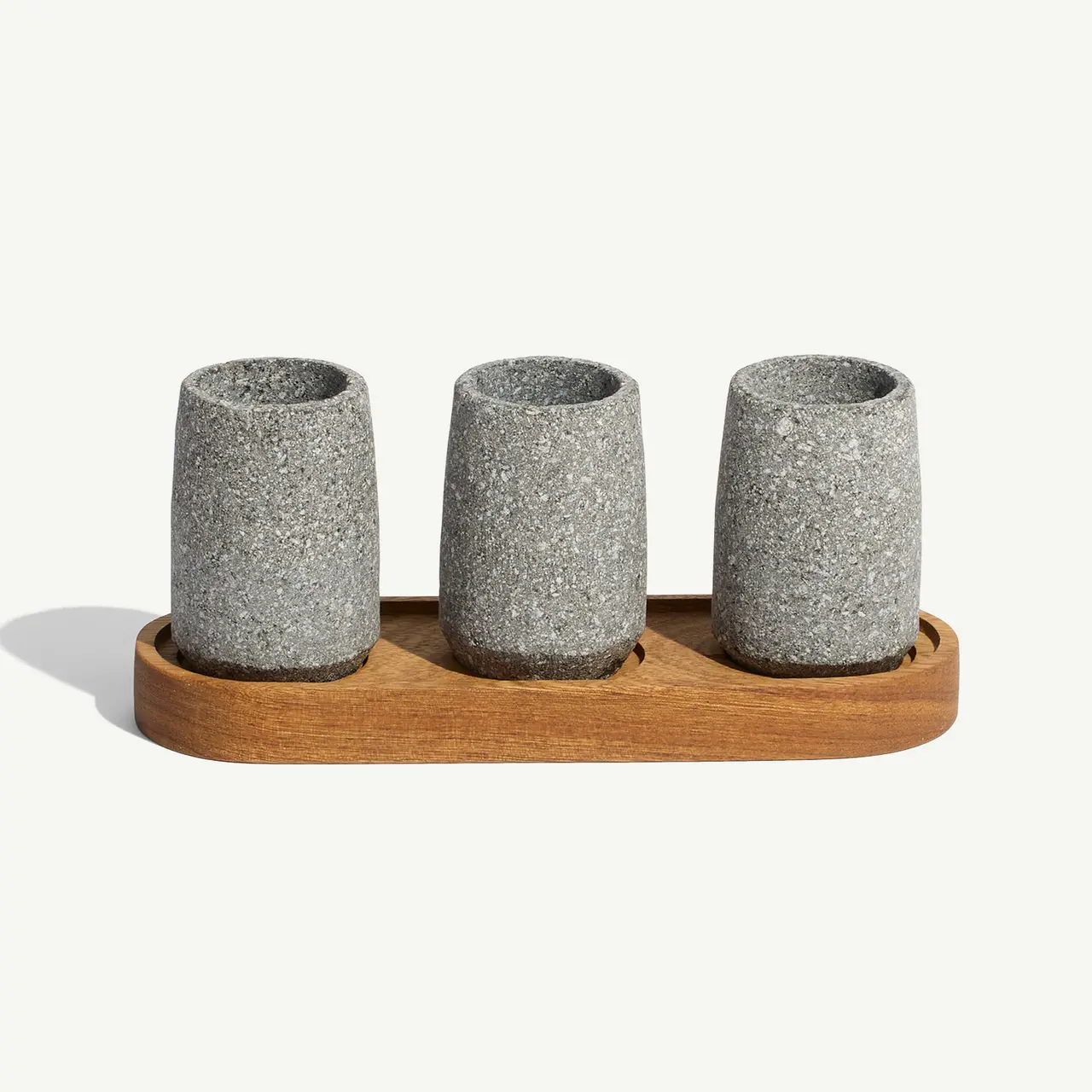 Three cylindrical stone cups sitting on a wooden tray against a plain background.