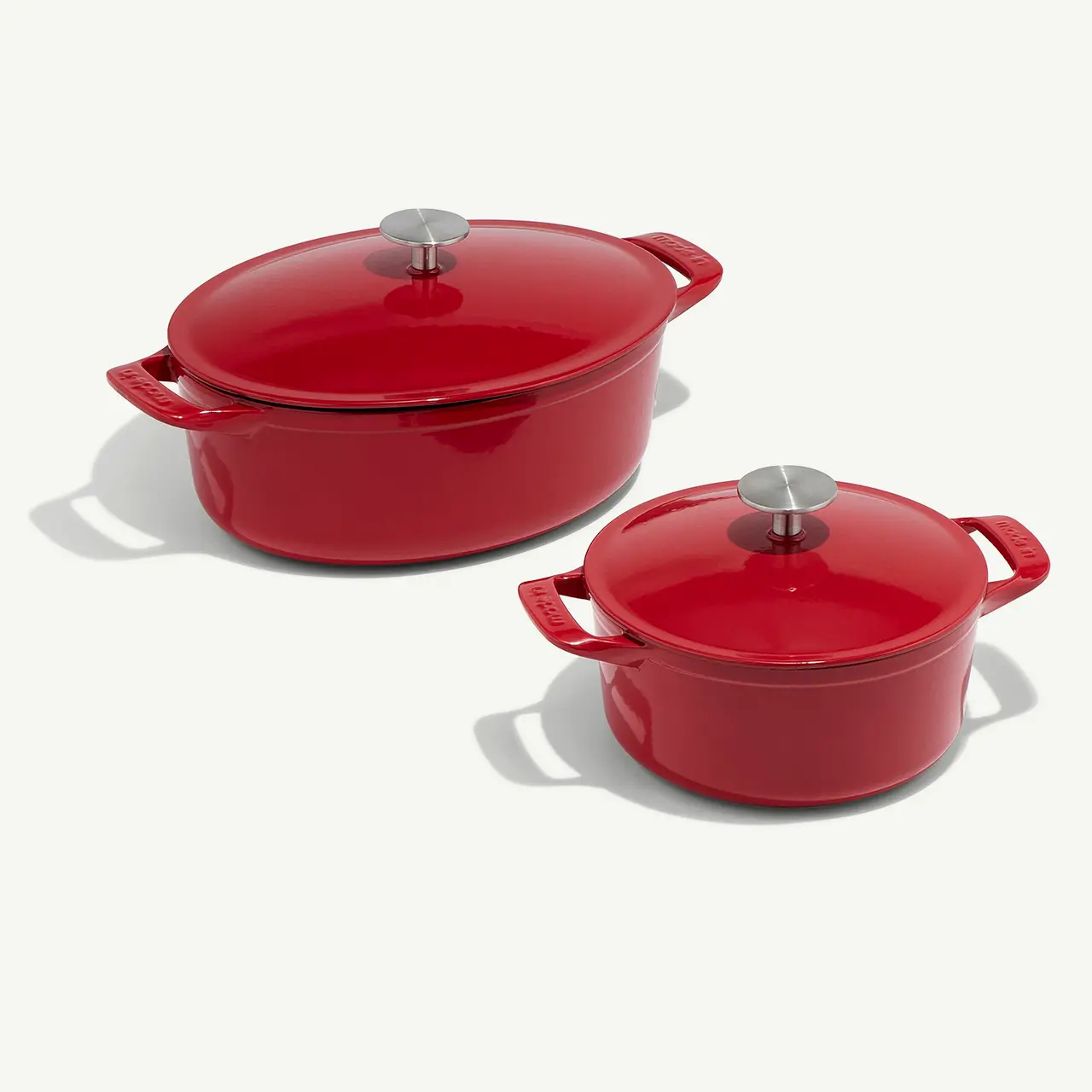 Two red enameled pots with lids, one larger than the other, sit side by side on a white surface.