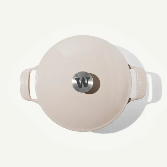 A beige Dutch oven with a stainless steel knob featuring a "W" logo sits against a light background.