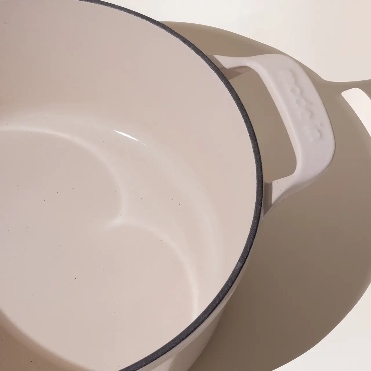 A close-up of a beige ceramic pan with a white interior and a black rim, highlighting its curved edge and handle.