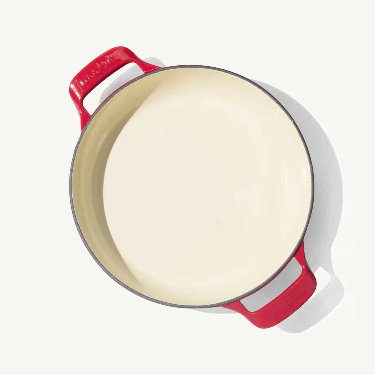 A round, red-handled cast iron pot with a smooth, light-colored interior sits on a neutral background.