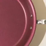 Close-up view of a burgundy non-stick frying pan with a portion of its metal handle visible.