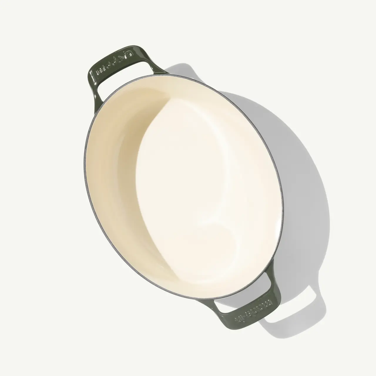 A round, shallow ceramic baking dish with green handles and a creamy beige interior.