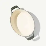 A round, shallow ceramic baking dish with green handles and a creamy beige interior.