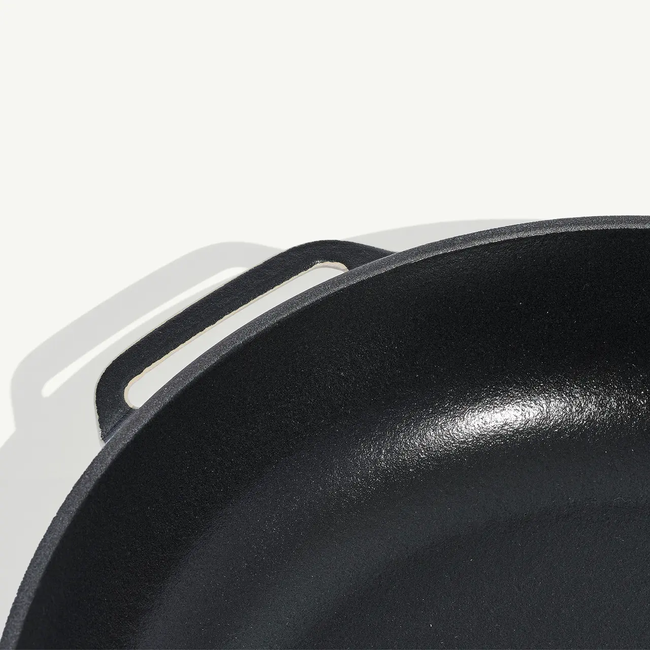 A close-up view of a black cast iron skillet on a white background, showcasing its handle and interior surface.