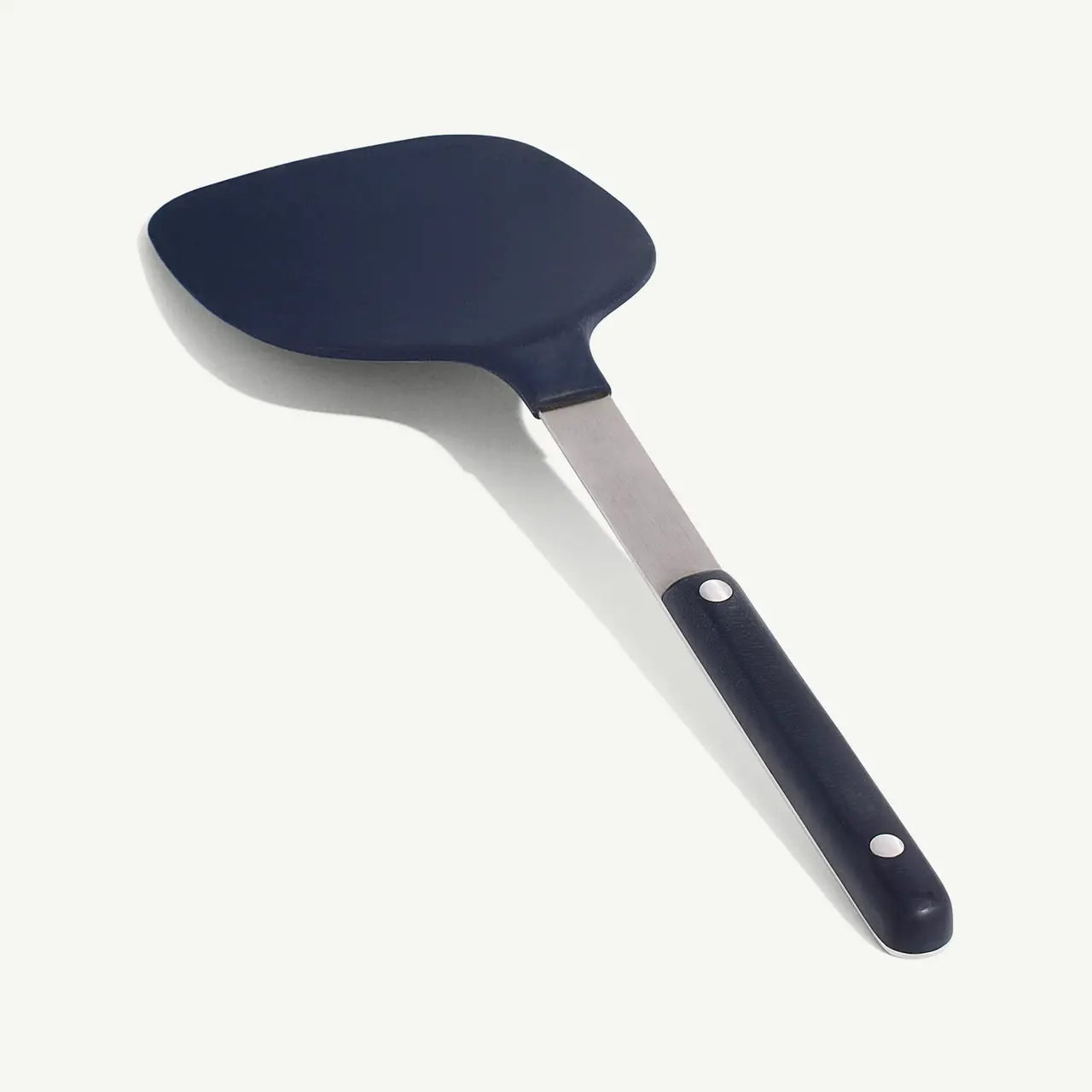A black spatula with a stainless steel handle and rivets lies against a white background.